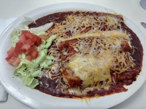 A plate of enchiladas topped with melted cheese, served with lettuce and diced tomatoes on the side.
