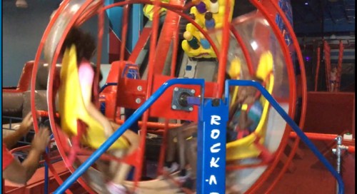 Children enjoying a colorful indoor play structure, spinning in a large transparent wheel.