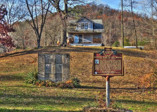 A historic site featuring a house on a hill, with informational plaques in the foreground and autumn foliage.
