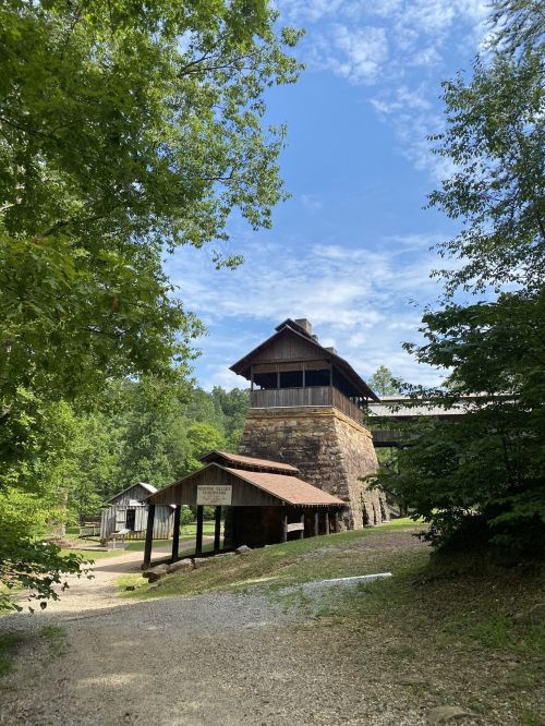 Historic stone building surrounded by trees under a blue sky, with a gravel path leading up to it.