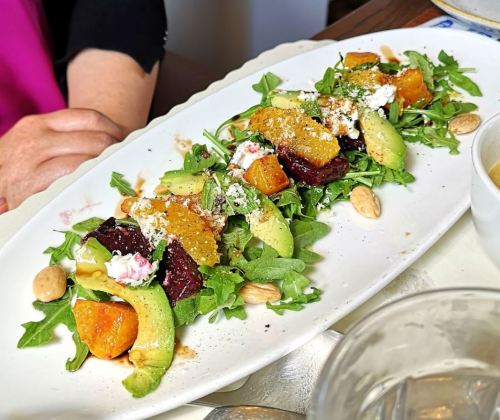 A vibrant salad with arugula, beets, avocado, roasted squash, goat cheese, and almonds on a white plate.