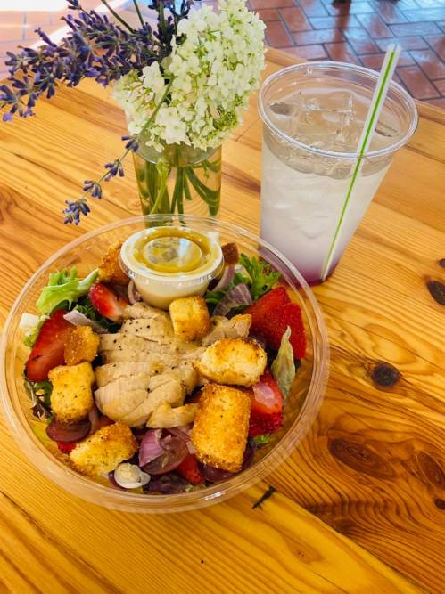 A colorful salad with chicken, strawberries, croutons, and dressing, alongside a drink and a small flower arrangement.