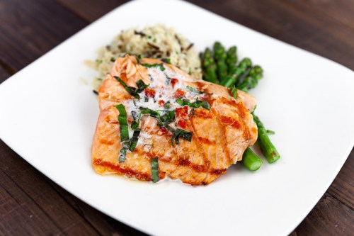 Grilled salmon fillet topped with herbs, served with asparagus and a side of rice on a white plate.