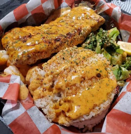 A plate featuring grilled fish topped with a creamy sauce, served with seasoned rice and mixed vegetables.