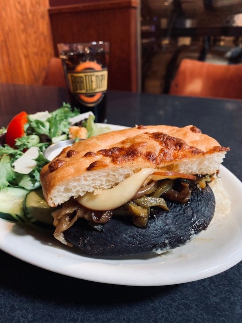 A hearty sandwich with melted cheese and sautéed vegetables on a toasted bun, served with a side salad.