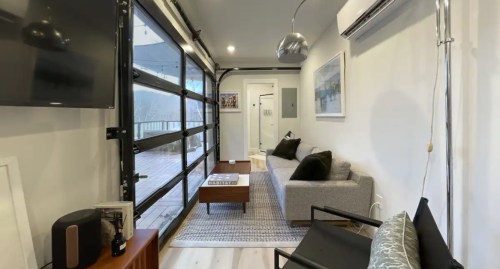Cozy living space with a gray sofa, coffee table, and large glass doors leading to a deck. Modern decor and lighting.