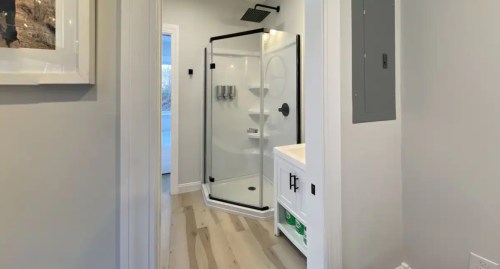 A modern bathroom featuring a glass shower enclosure and light wood flooring, with a vanity and wall-mounted fixtures.