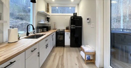 Modern kitchen with wooden countertops, black appliances, and large windows overlooking a natural landscape.