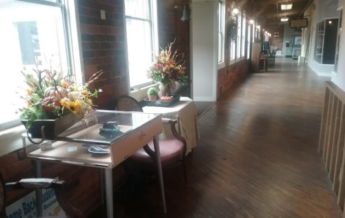 A cozy hallway with wooden floors, featuring a table with flowers and a chair, leading to other rooms.