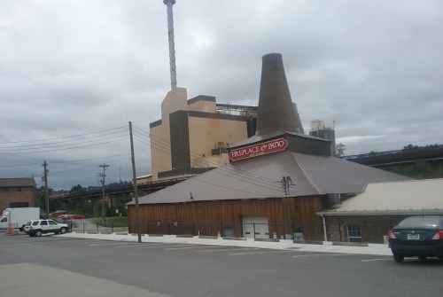 A rustic building with a chimney, labeled "Fireplace & Patio," set against a cloudy sky and industrial backdrop.
