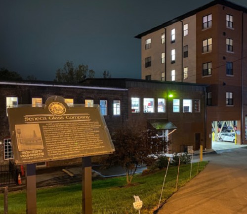 A historic sign for Seneca Glass Company in front of a modern building at night, with illuminated windows.