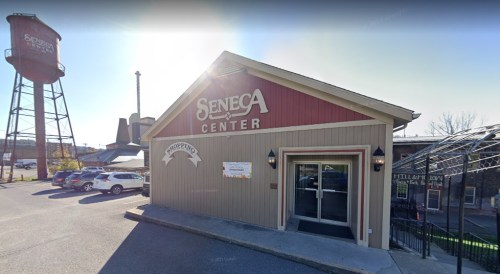 Exterior of the Seneca Center building with a sign, parking lot, and water tower in the background on a sunny day.