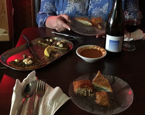 A table set with plates of food, a bottle of wine, and a glass of red wine, with a person holding a plate.