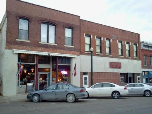 Historic brick building with storefronts, featuring large windows and parked cars in front.