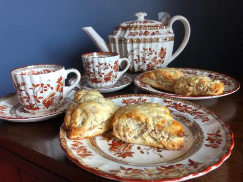 A teapot and cups on a wooden table, with plates of scones decorated in floral patterns.
