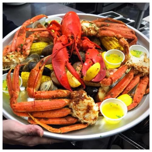A large platter of seafood featuring lobster, crab, clams, corn, and dipping sauces, garnished with herbs.