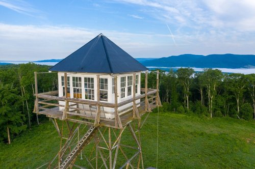 A wooden observation tower with a black roof, surrounded by trees and overlooking a scenic landscape.