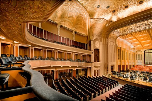 Interior of a grand concert hall featuring ornate architecture, tiered seating, and a stage set for a performance.