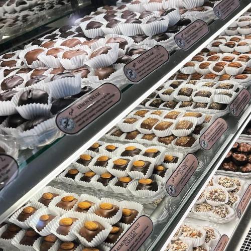 A display case filled with assorted chocolates and confections, each in paper cups, labeled with names.