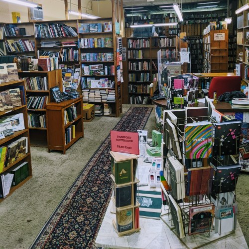 A cozy bookstore interior filled with shelves of books, a central display, and a patterned rug on the floor.