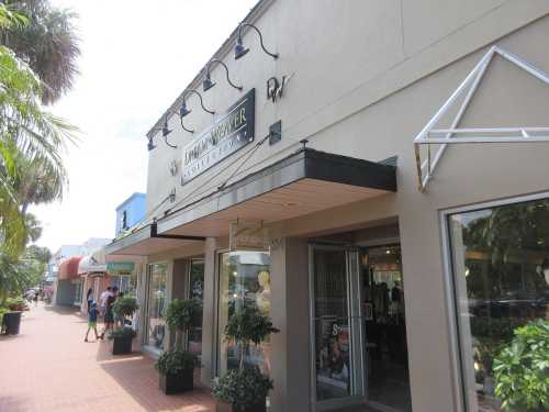 Storefront of a clothing shop with large windows, planters, and a sign reading "Tommy Hilfiger." Sunny day.