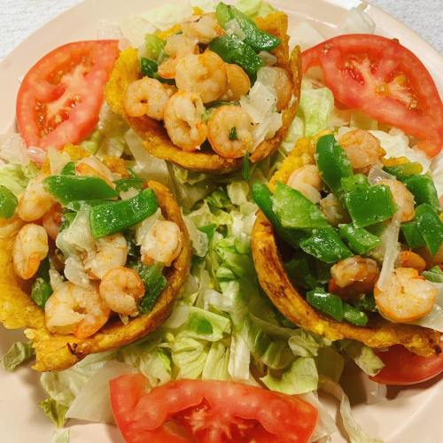 Three shrimp-filled taco cups on a bed of lettuce, garnished with green peppers and tomato slices.