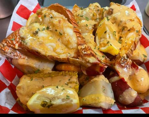 A close-up of a seafood dish featuring lobster claws, potatoes, and lemon, all drizzled with a creamy sauce.