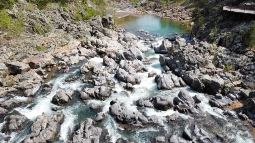 Aerial view of a rocky riverbed with flowing water and lush greenery along the banks.