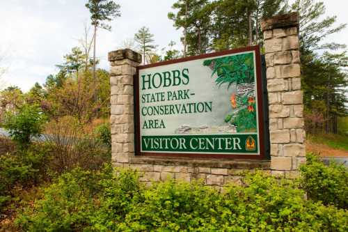 Sign for Hobbs State Park Conservation Area Visitor Center, surrounded by trees and greenery.