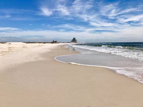 A serene beach scene with soft sand, gentle waves, and a distant skyline under a blue sky with wispy clouds.
