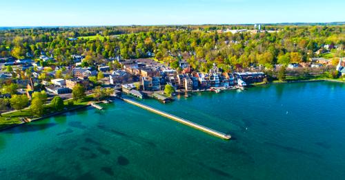 Aerial view of a lakeside town with green trees, buildings, and a long pier extending into the clear blue water.