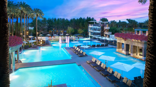 A luxurious pool area with lounge chairs, palm trees, and a vibrant sunset sky in the background.