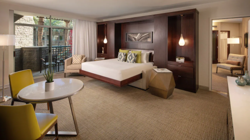 A modern hotel room featuring a king bed, seating area, and balcony access, with stylish decor and warm lighting.