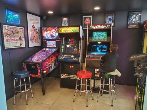 A cozy arcade corner with vintage games, including pinball machines and an arcade cabinet, and a child playing.