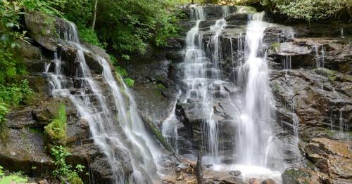 A serene waterfall cascading over rocky terrain, surrounded by lush green foliage.