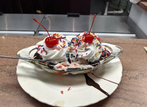 A delicious ice cream sundae with whipped cream, sprinkles, and cherries, served in a glass dish.