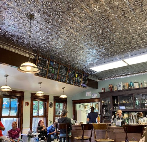 A cozy café interior with a decorative tin ceiling, menu boards, and patrons enjoying their time at the counter.