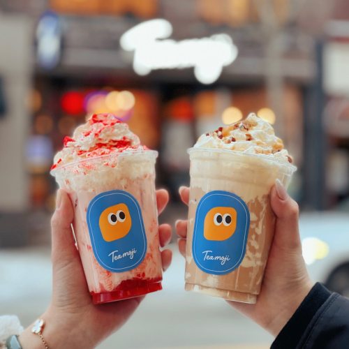 Two hands hold colorful drinks topped with whipped cream and syrup, featuring playful logos on the cups.