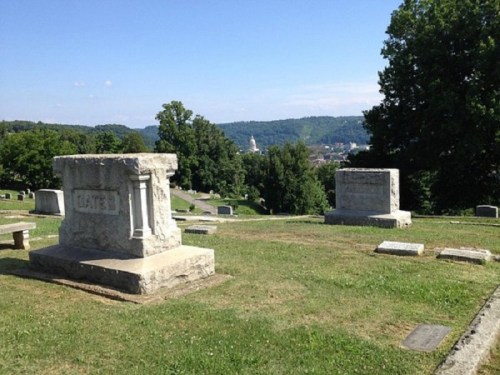 A peaceful cemetery scene with gravestones on a grassy hill, overlooking a distant landscape and blue sky.