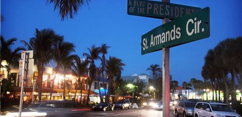 Street sign at dusk for St. Armands Circle, with palm trees and shops illuminated in the background.