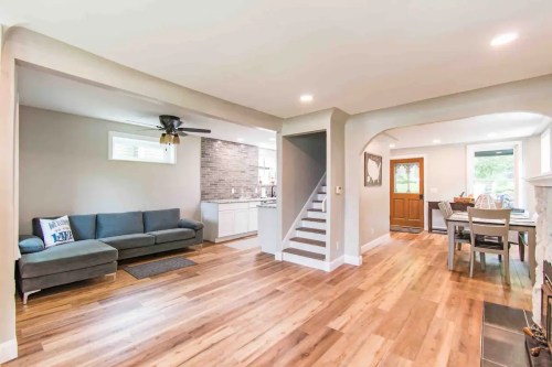 A modern living space featuring a gray couch, wooden floors, a dining area, and a staircase leading to an upper level.