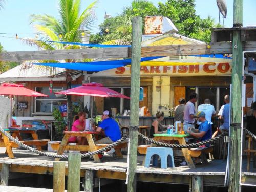 A lively outdoor dining area with umbrellas, people enjoying meals, and a colorful restaurant in the background.