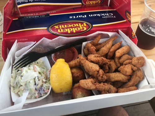 A box of fried chicken wings with coleslaw, a lemon wedge, and dipping sauce, alongside a drink.