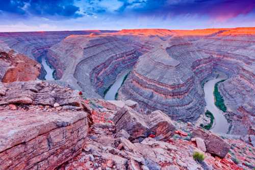 A stunning view of a winding river through layered rock formations at sunset, with vibrant colors in the sky.