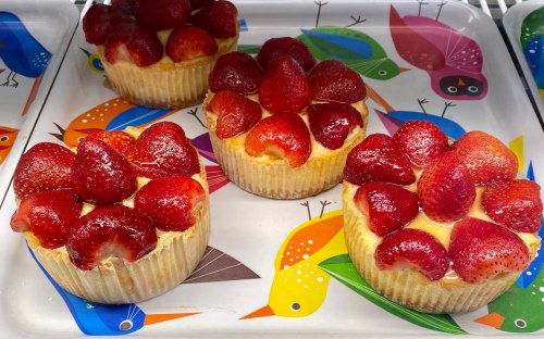 Four strawberry-topped cupcakes on a colorful bird-patterned tray.