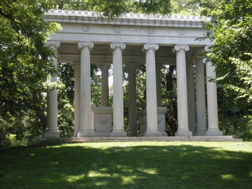 A classical stone monument with columns, surrounded by lush greenery, featuring the name "Palmer" inscribed on it.