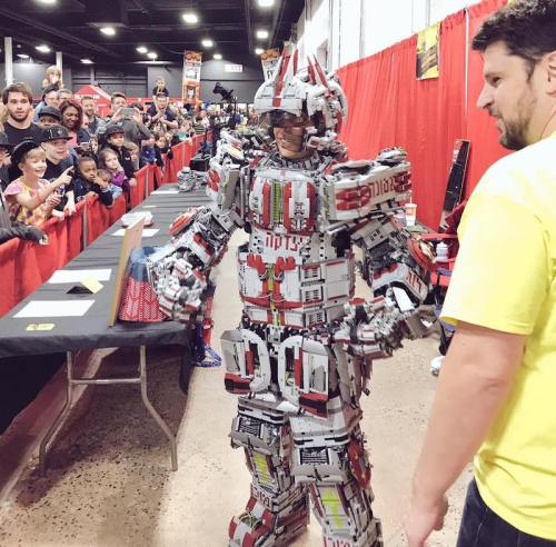 A person in a detailed, colorful robot costume made of building blocks stands in front of an excited crowd at an event.