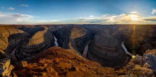 A panoramic view of a canyon with winding river, rocky cliffs, and a sunset illuminating the landscape.