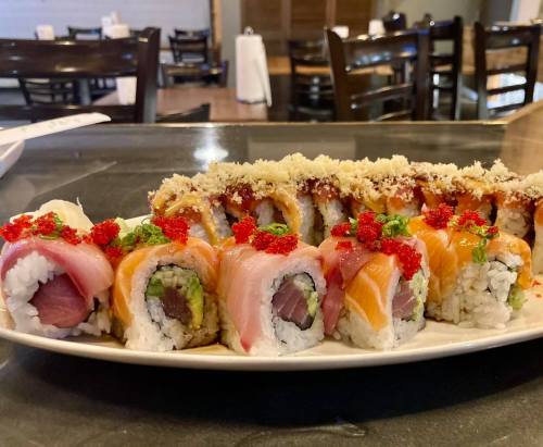 A platter of colorful sushi rolls, featuring various toppings like fish, avocado, and roe, on a black table.