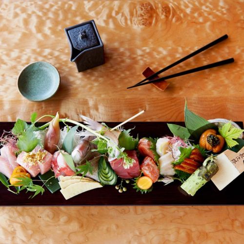 A beautifully arranged sushi platter with various sashimi, garnishes, and a small dish, set on a wooden table.